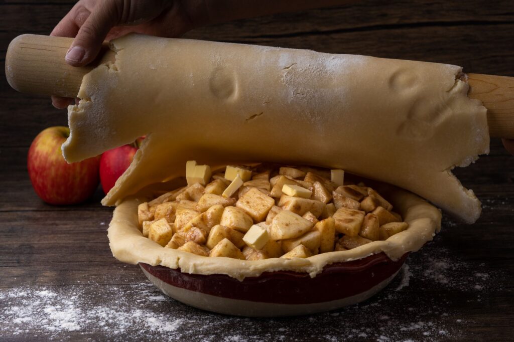 Étaler de la pâte pour une tarte aux pommes maison avec des morceaux de pomme frais et une croûte beurrée.