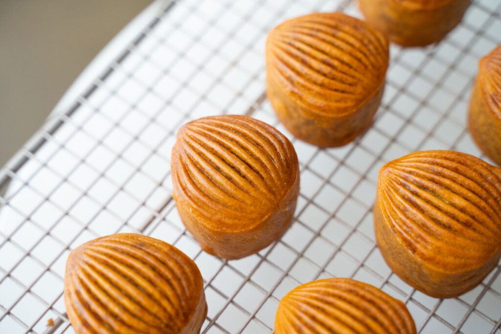 Des pâtisseries en forme de coquillage dorées en train de refroidir sur une grille. Parfait pour les amateurs de desserts.