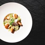 Vue aérienne d'une salade de crevettes et avocat fraîchement présentée sur une assiette blanche contre un fond texturé noir.