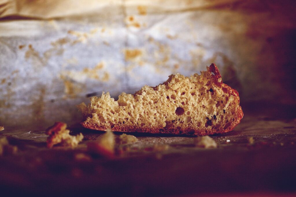Gros plan de la miette de pain brun rustique sur du papier de cuisson texturé, évoquant chaleur et simplicité.