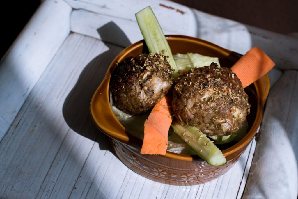 Boules de viande savoureuses maison avec des tranches de concombre et de carotte dans un bol rustique.