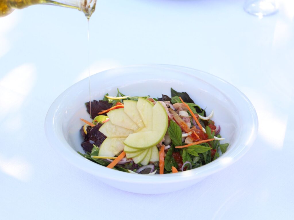 Salade colorée de pommes dans un bol blanc avec un filet d'huile d'olive, débordant de légumes frais.