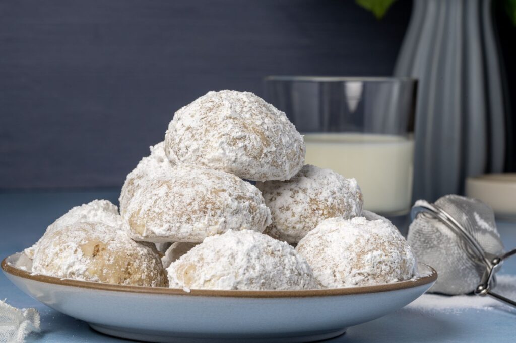 Délicieux kourabiedes saupoudrés de sucre glace sur une assiette en céramique, parfaits pour les célébrations.