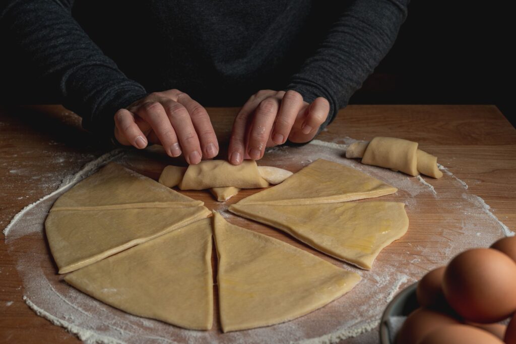 Gros plan sur des mains roulant de la pâte en croissants sur une surface farinée.