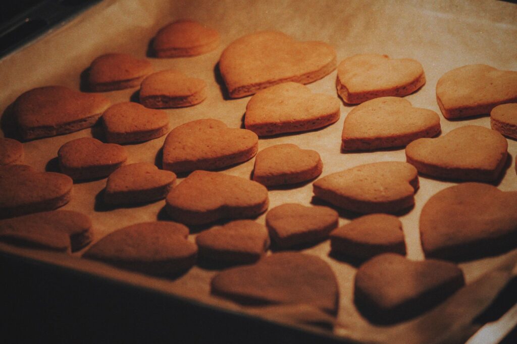 Gros plan de biscuits en forme de cœur fraîchement cuits sur une plaque à pâtisserie tapissée de papier sulfurisé.