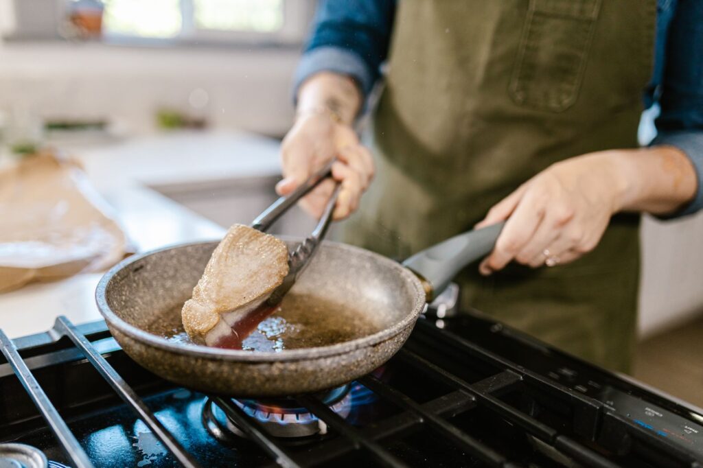 Gros plan sur un chef faisant frémir un steak de thon avec des pinces dans une poêle sur une cuisinière à gaz.