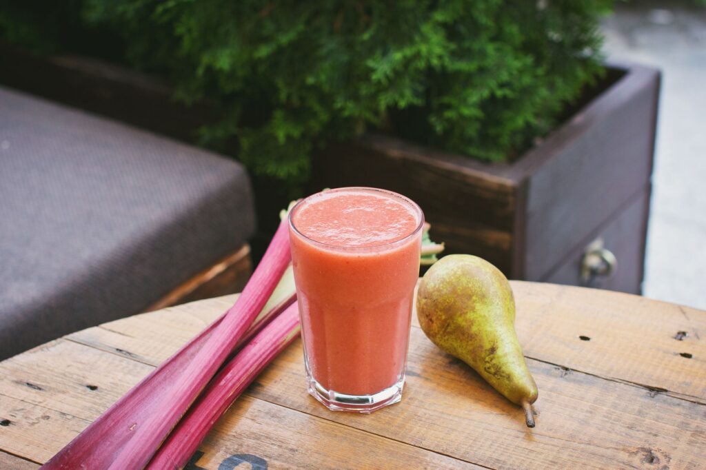 Délicieux smoothie poire et rhubarbe dans un verre sur une table en bois, parfait pour une rafraîchissement d'été.