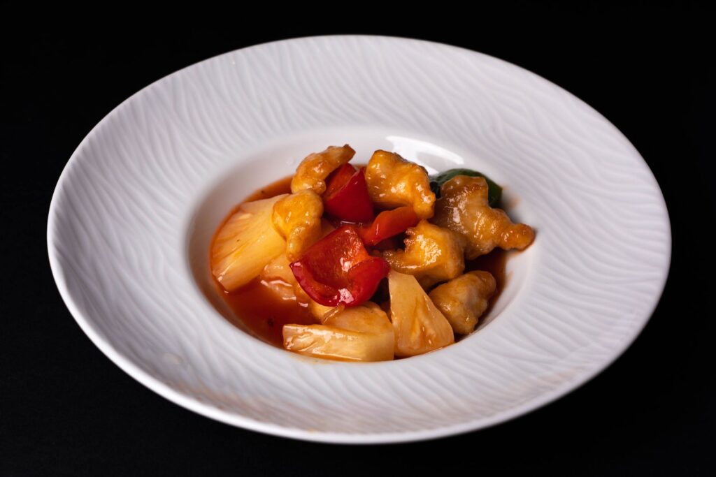 Gros plan sur du poulet aigre-doux avec des poivrons et de l'ananas sur une assiette en céramique.