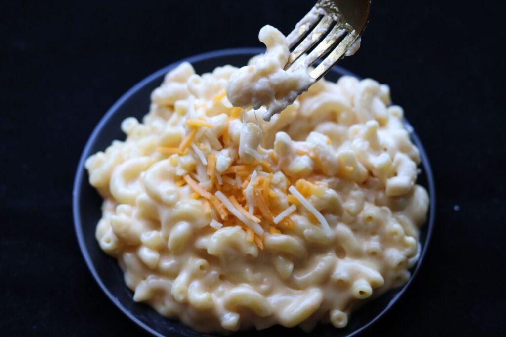 Délicieuse mac and cheese crémeuse garnie de fromage râpé sur une assiette noire.