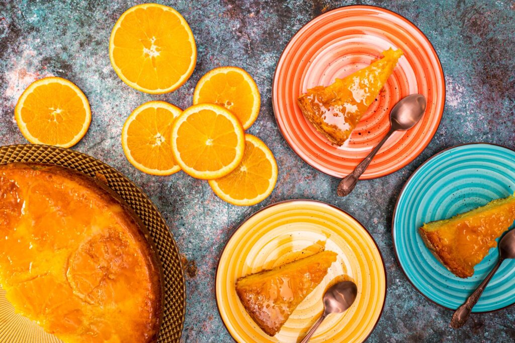 Vue rapprochée de tranches de gâteau à l'orange sur des assiettes colorées avec des tranches d'orange fraîches.