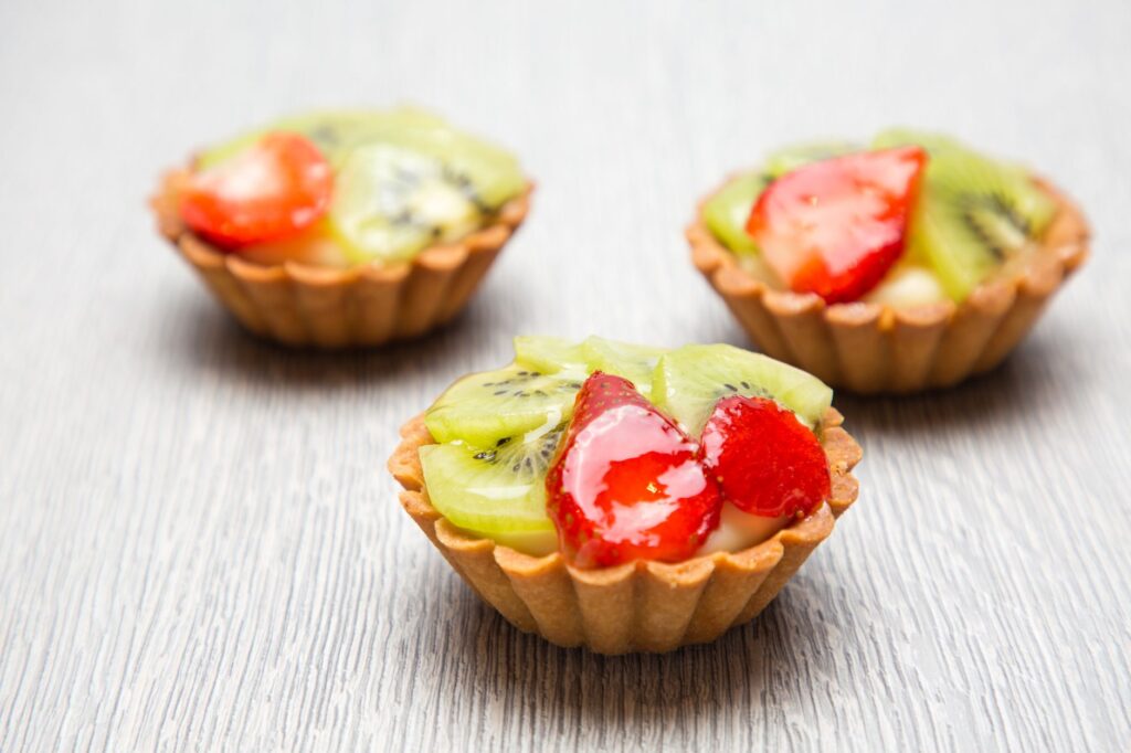 Gros plan sur trois tartes aux fruits frais garnies de tranches de kiwi et de fraise sur une table en bois.