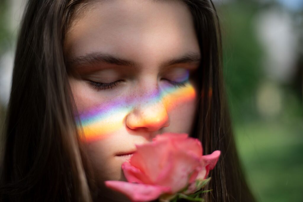 Un portrait serein d'une jeune femme avec une lumière arc-en-ciel sur son visage, tenant une rose rose.