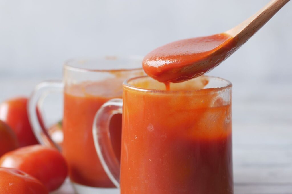 Gros plan de sauce tomate dans des verres avec des tomates à côté.