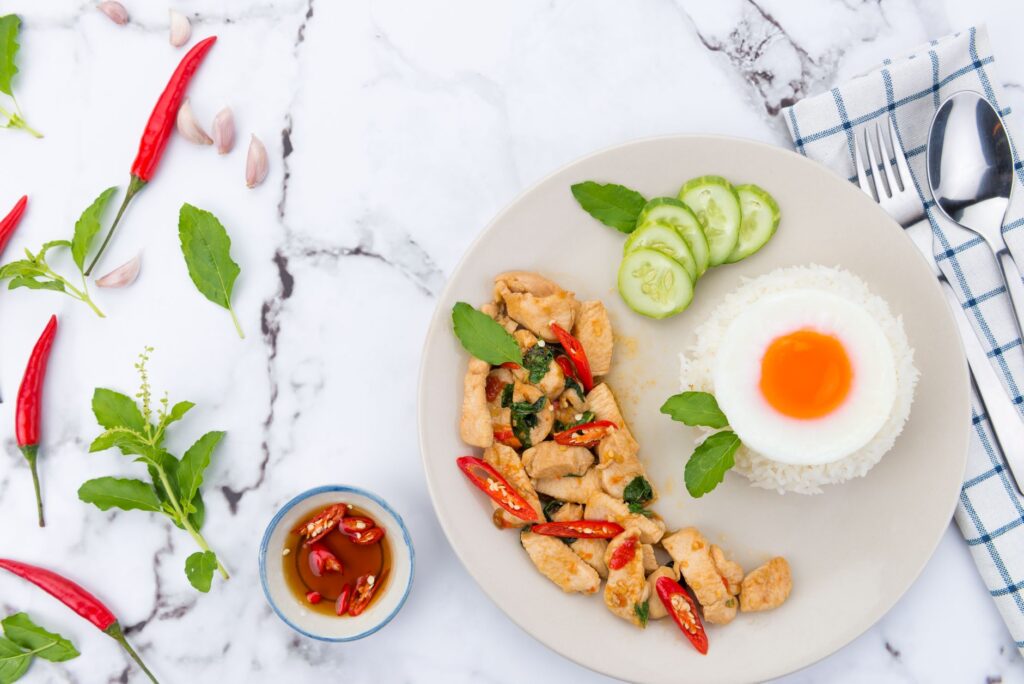 Vue de dessus d'un repas thaïlandais avec œuf frit, poulet au basilic, servi sur marbre avec piment et concombre.