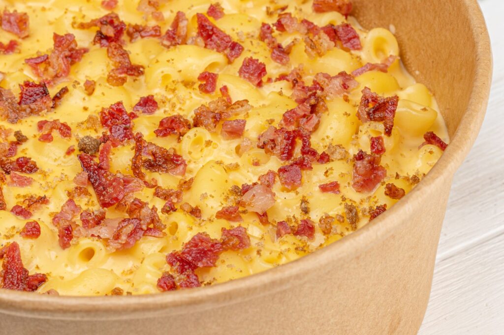Savourez ce délicieux macaron au bacon et fromage dans un bol en papier rustique, parfait pour les amateurs de comfort food.