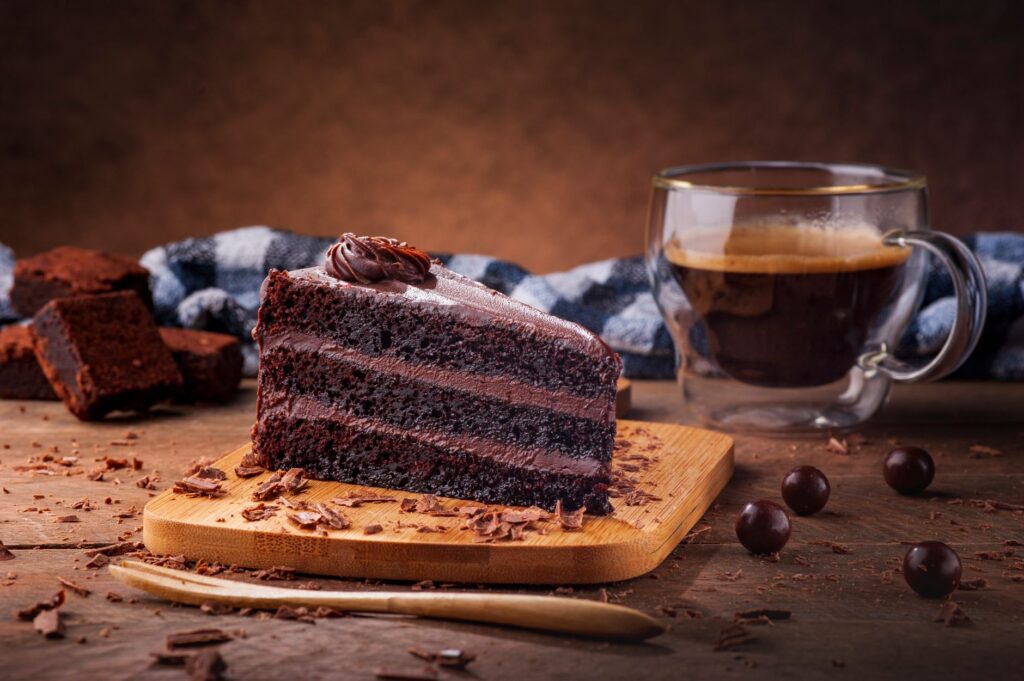 Une tranche de gâteau au chocolat riche sur une planche en bois avec un café espresso pour une douce gourmandise.