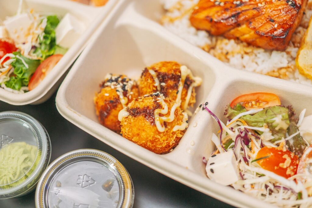 Gros plan sur une boîte bento avec du saumon grillé, du riz, de la salade et des croquettes.