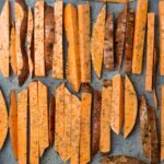 Gros plan de patates douces tranchées assaisonnées et disposées sur une plaque de cuisson avec du papier sulfurisé.