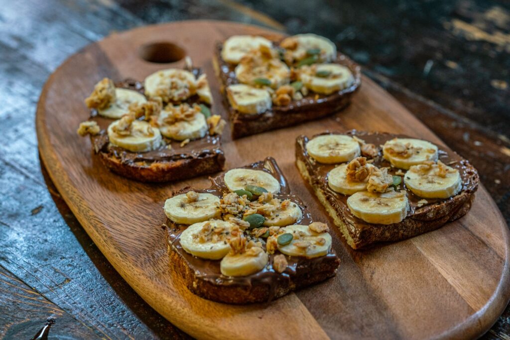 Gros plan sur des toasts à la banane et au Nutella garnis de granola sur une planche en bois.