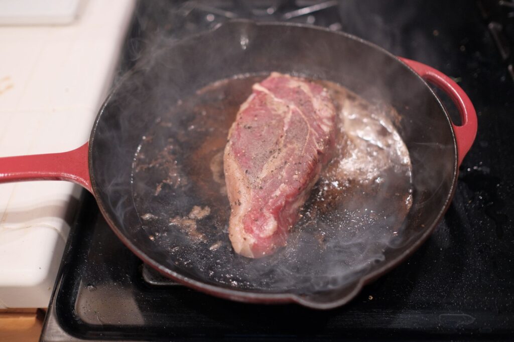 Gros plan sur un steak grésillant dans une poêle en fonte sur une cuisinière.