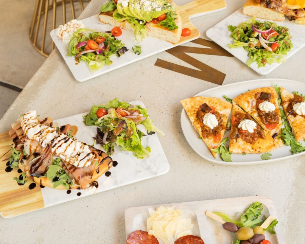 Une sélection appétissante de plats de déjeuner gourmet incluant des salades, des sandwiches et des plateaux de fromage.