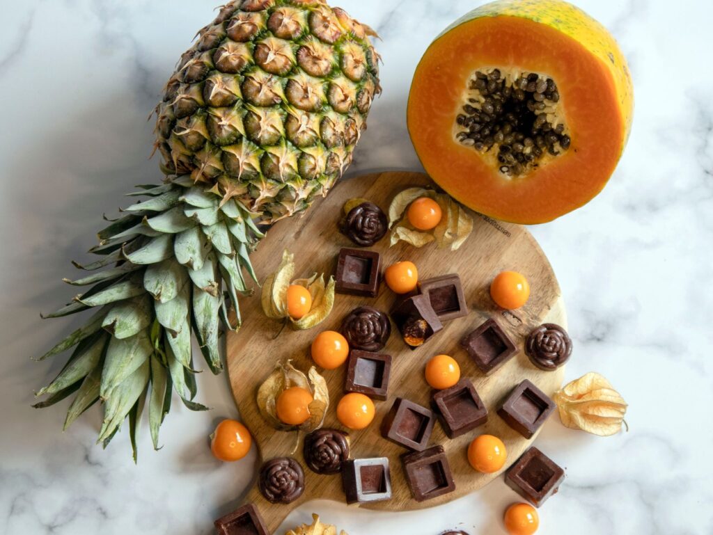 Une présentation vibrante d'ananas, de papaye et de chocolats variés sur une planche en bois et une surface en marbre.