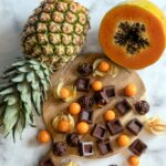 Une présentation vibrante d'ananas, de papaye et de chocolats variés sur une planche en bois et une surface en marbre.