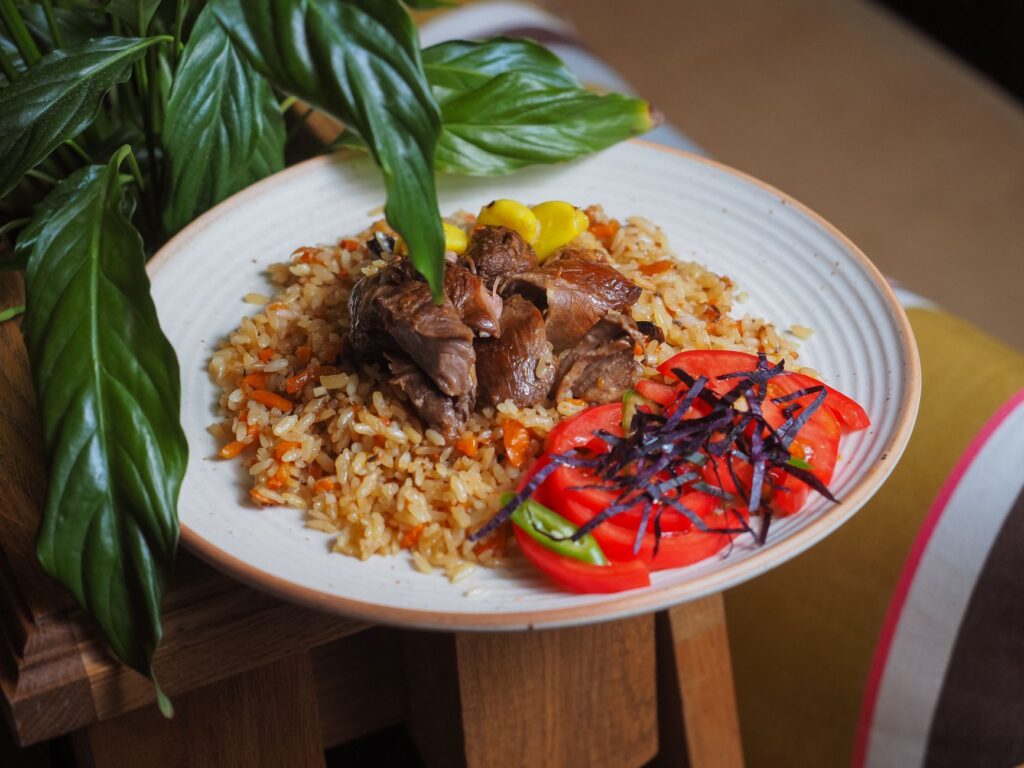 Gros plan d'un délicieux plat de pilaf garni de viande juteuse, de tomates et de légumes verts sur une assiette rustique.
