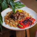 Gros plan d'un délicieux plat de pilaf garni de viande juteuse, de tomates et de légumes verts sur une assiette rustique.
