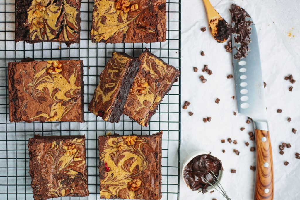 Délicieuses brownies au chocolat avec des noix sur une grille de refroidissement et un couteau sur fond blanc.