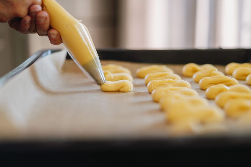 Un gros plan de pâte étant pipée sur du papier sulfurisé, mettant en avant l'art de la pâtisserie.
