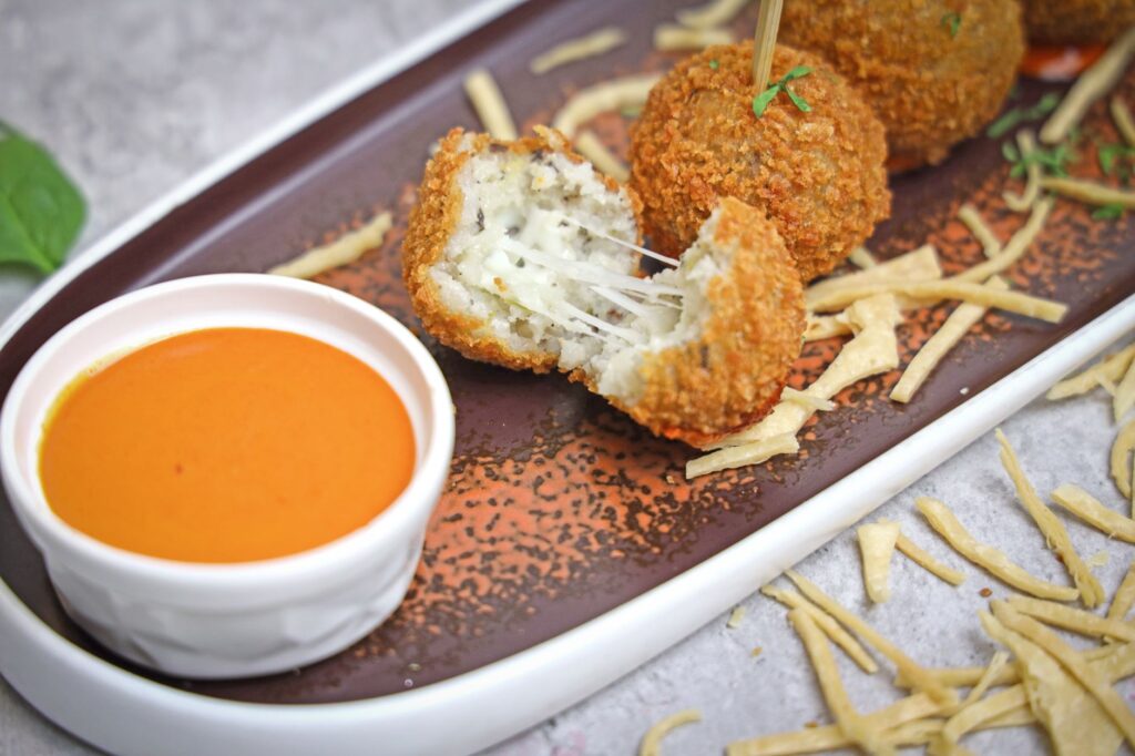 Croustillantes croquettes de fromage servies avec une sauce tomate acidulée sur une assiette décorative.