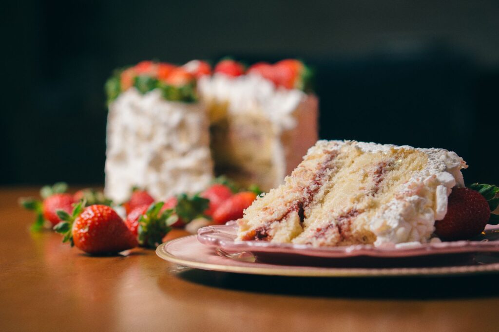 Gros plan sur une part de gâteau aux fraises avec de la crème fouettée et des fraises fraîches dans une assiette rose.