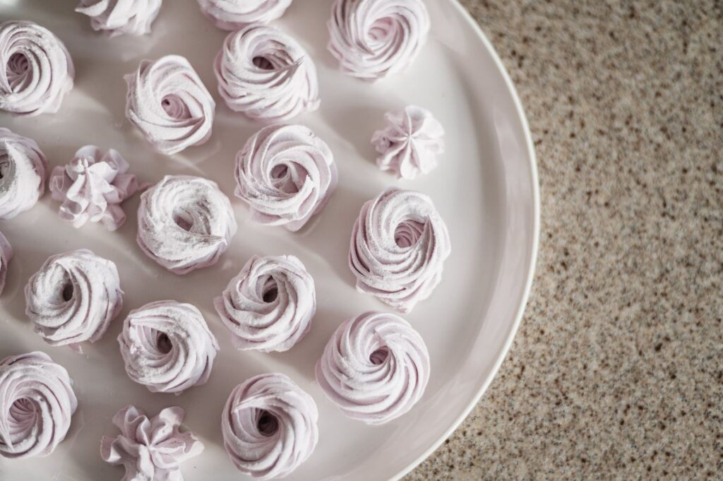 Vue de dessus de meringues roses pastel disposées sur une assiette blanche pour une présentation de douceurs.