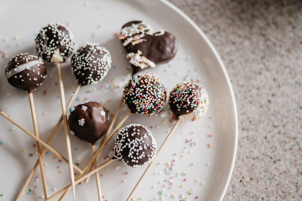 Gros plan sur des cake pops au chocolat avec des vermicelles colorés sur une assiette.