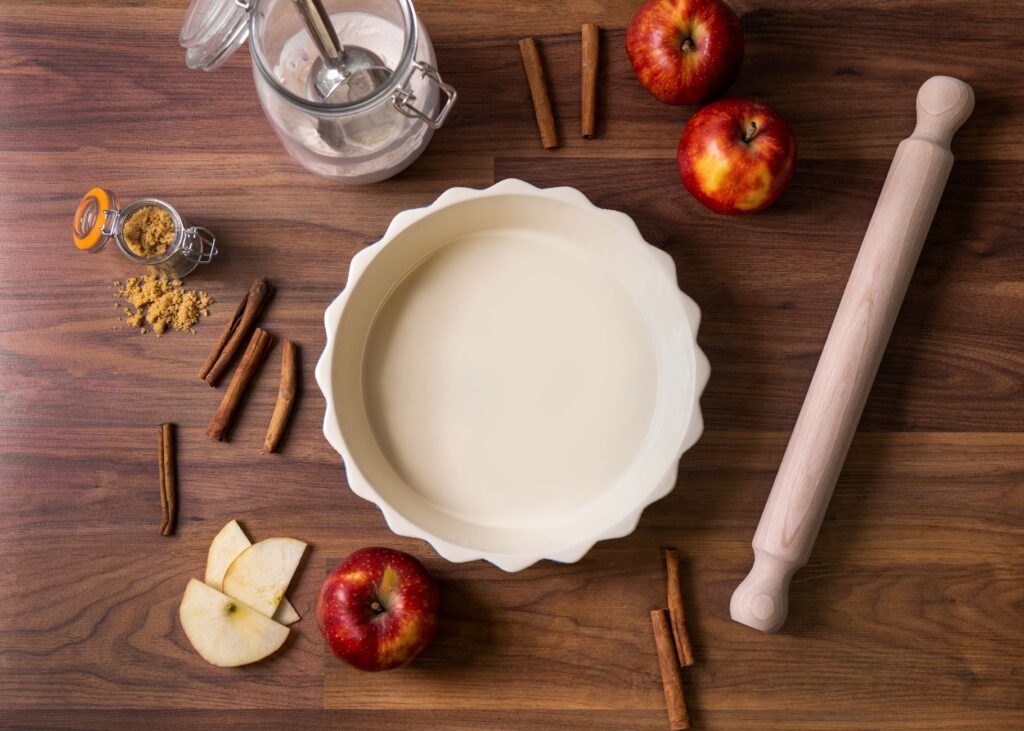 Vue d'ensemble des ingrédients pour une tarte aux pommes, y compris des pommes, des bâtons de cannelle et un rouleau à pâtisserie.