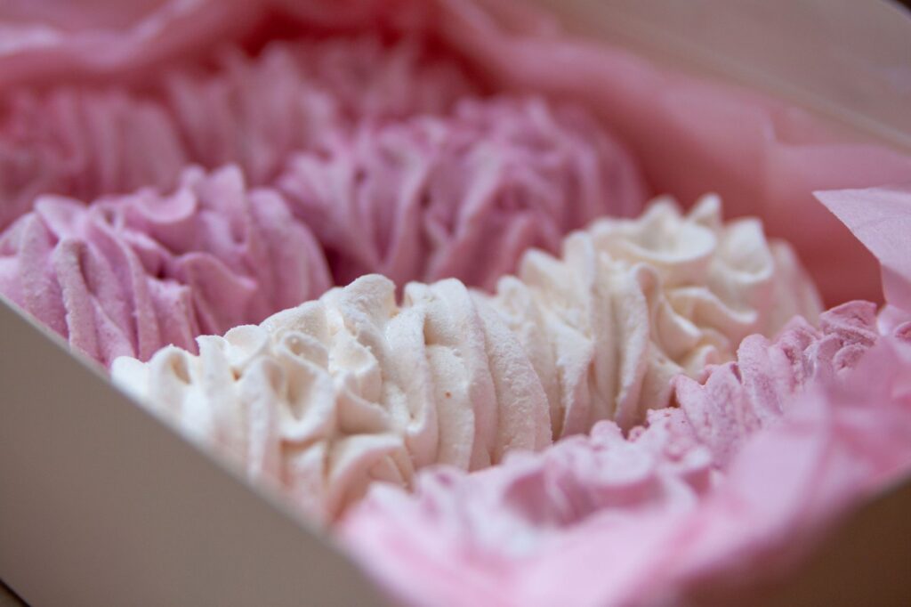 Gros plan sur des meringues roses et blanches dans une boîte, parfaites pour les gourmands.