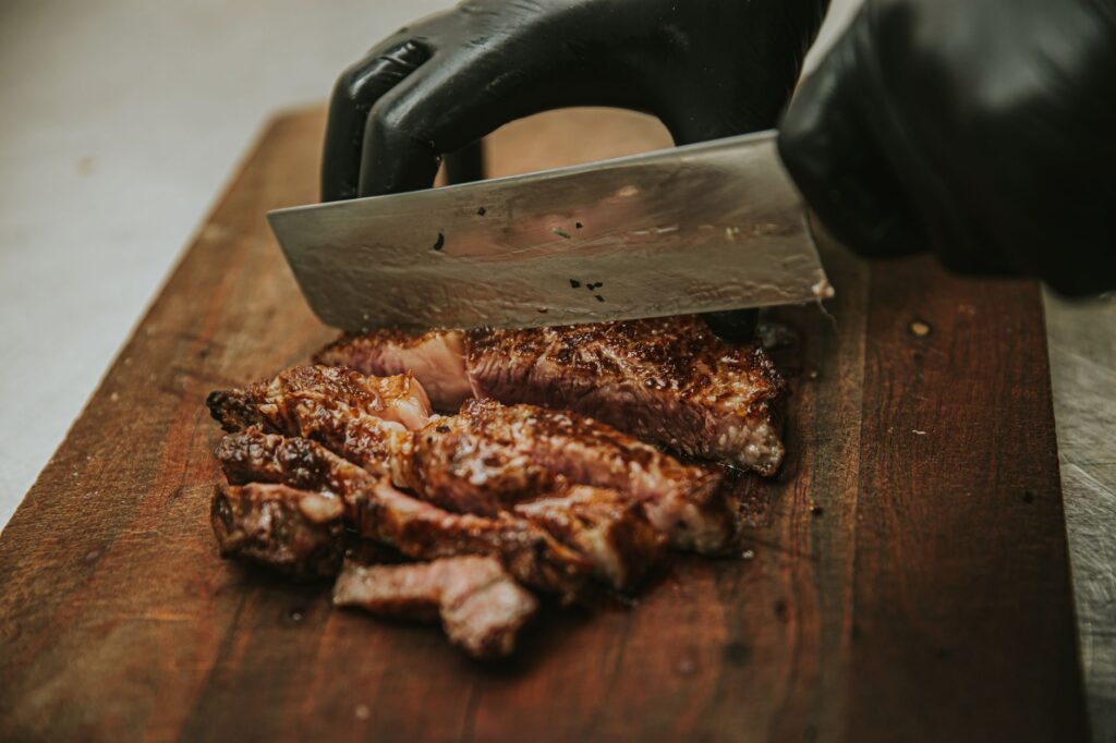 Gros plan sur un chef tranchant un steak grillé juteux sur une planche à découper en bois avec un couteau de cuisine.