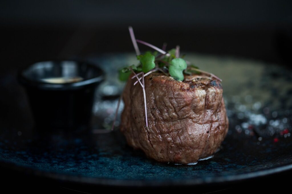 Un steak grillé succulent surmonté de micro-pousses servi dans une assiette sombre pour un repas gourmet.