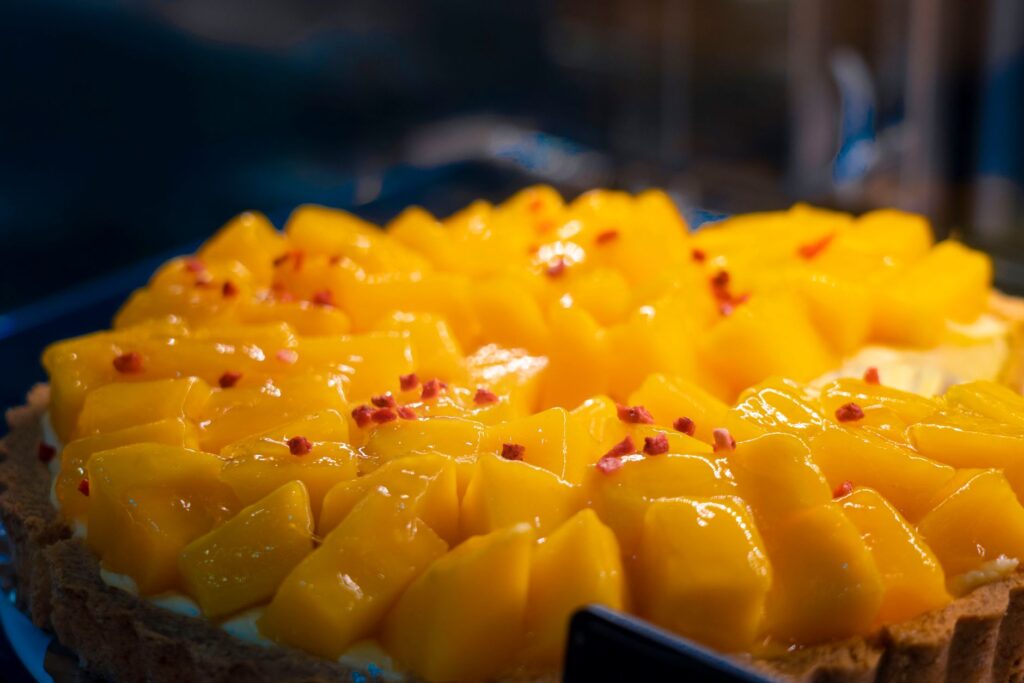 Gros plan sur une tarte à la mangue garnie de tranches de fruits jaunes éclatants et décorée de specks rouges.