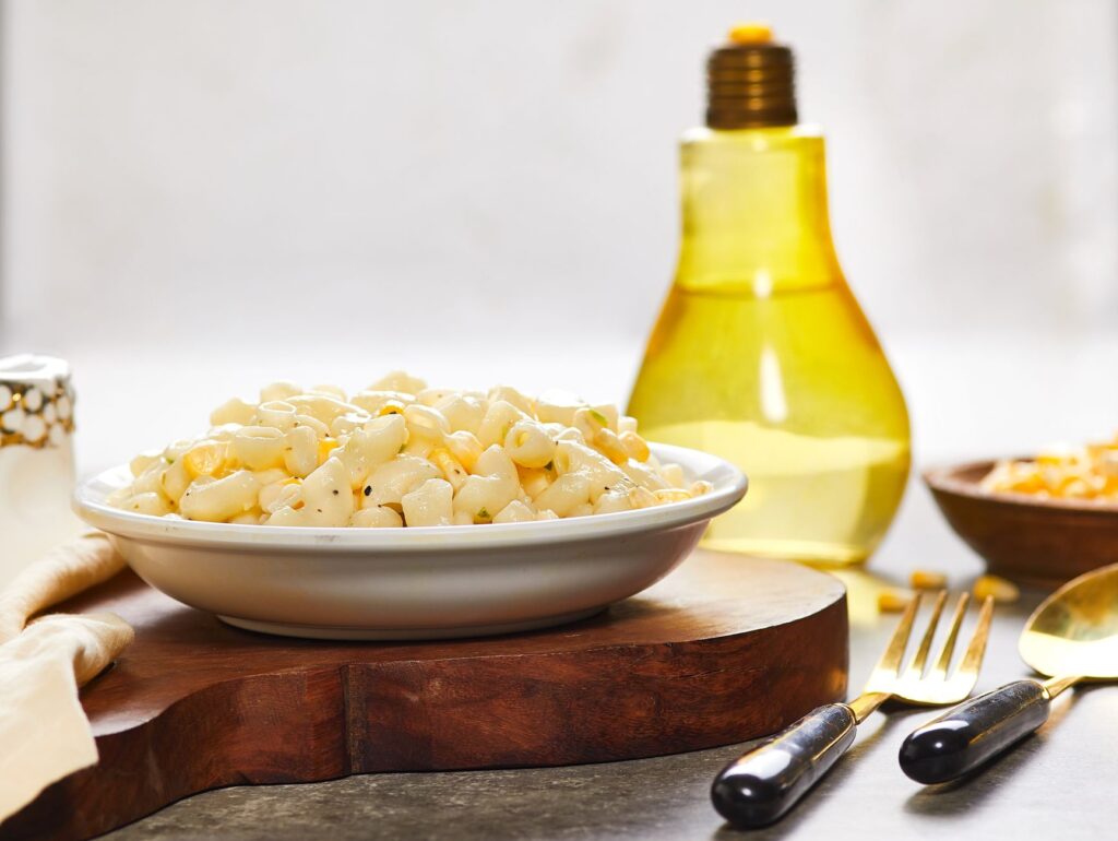 Délicieux bol de macaronis avec une sauce blanche crémeuse, de l'huile d'olive et du maïs sur une planche en bois rustique.