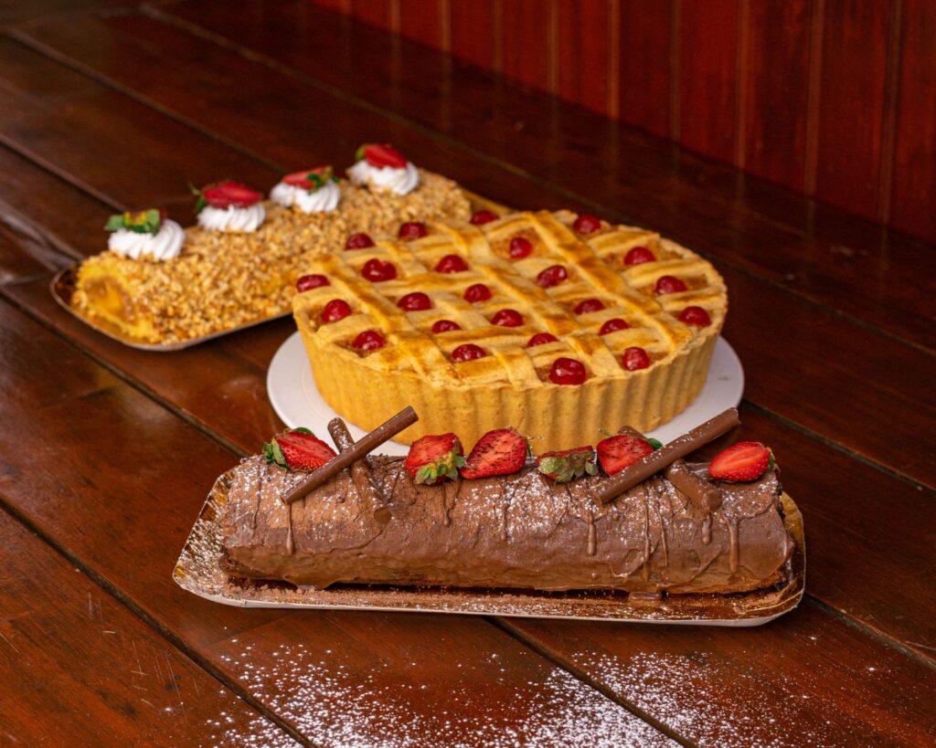 Un affichage tentant de pâtisseries comprenant une bûche au chocolat, une tarte aux fruits et un gâteau aux noix sur une table en bois.