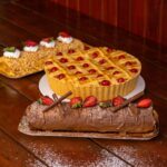 Un affichage tentant de pâtisseries comprenant une bûche au chocolat, une tarte aux fruits et un gâteau aux noix sur une table en bois.