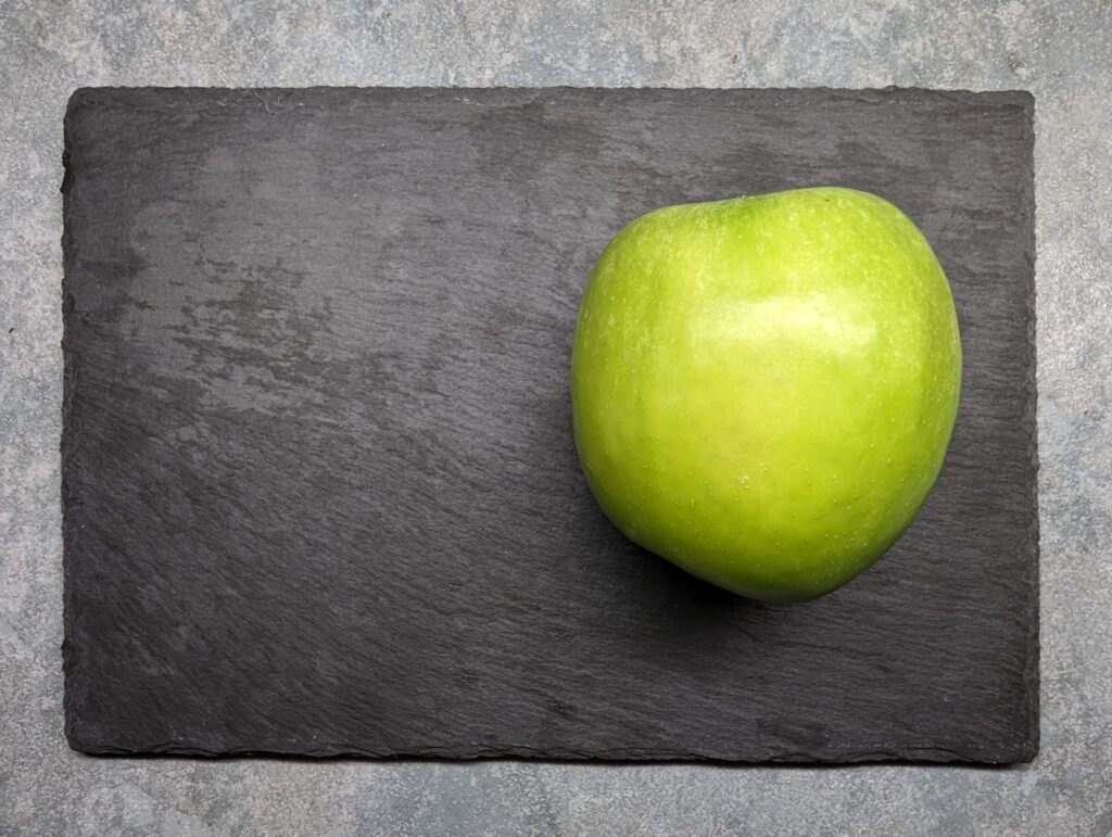 Une pomme Granny Smith fraîche placée sur une planche en ardoise sombre, mettant en avant la simplicité et la fraîcheur.