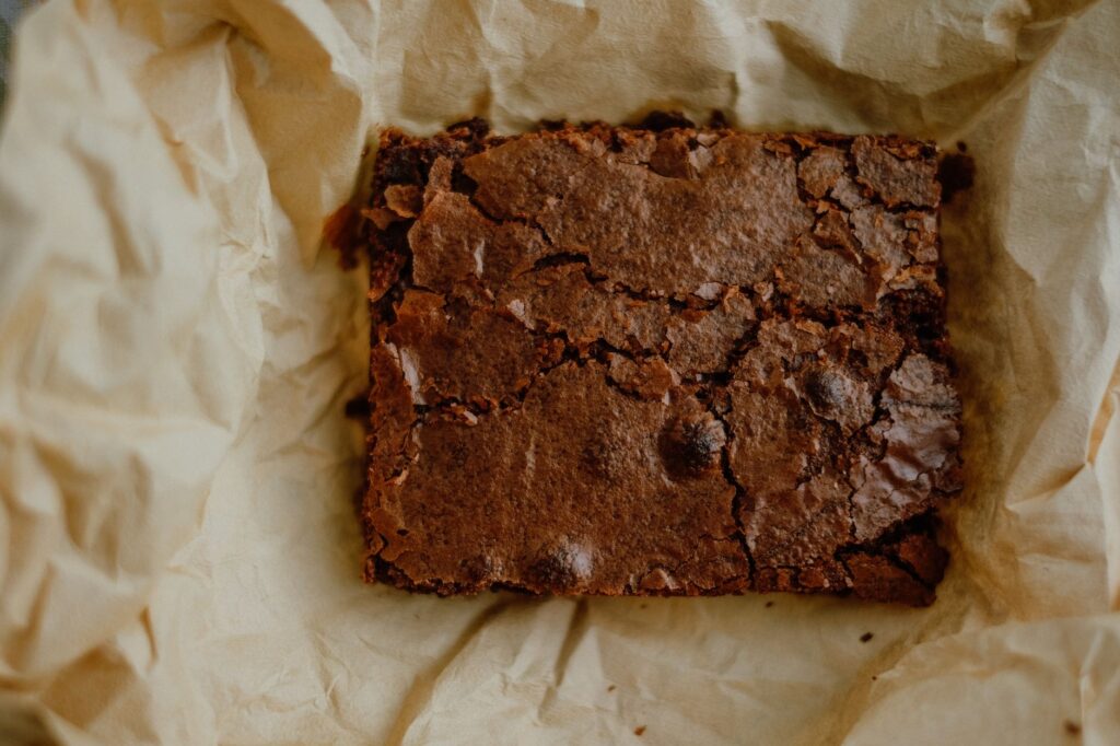 Gros plan sur un brownie au chocolat fraîchement cuit reposant sur du papier parchemin, parfait pour les amateurs de desserts.