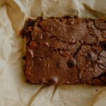 Gros plan sur un brownie au chocolat fraîchement cuit reposant sur du papier parchemin, parfait pour les amateurs de desserts.