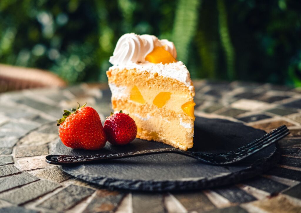 Une délicieuse part de gâteau aux fruits surmontée de crème, accompagnée de fraises fraîches et d'une fourchette sur une assiette en pierre.