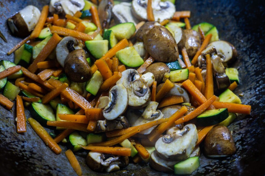 Gros plan sur des légumes sautés vibrants, y compris des champignons, des carottes et des courgettes dans un wok.