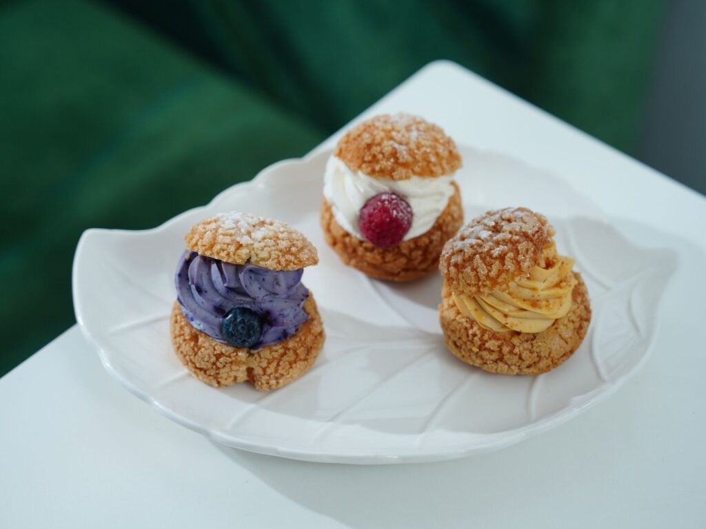 Trois choux à la crème avec des garnitures colorées et des fruits sur une assiette décorative.