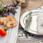 Pain tranché, tomates fraîches et fromage avec des graines de sésame noir dans une présentation rustique.